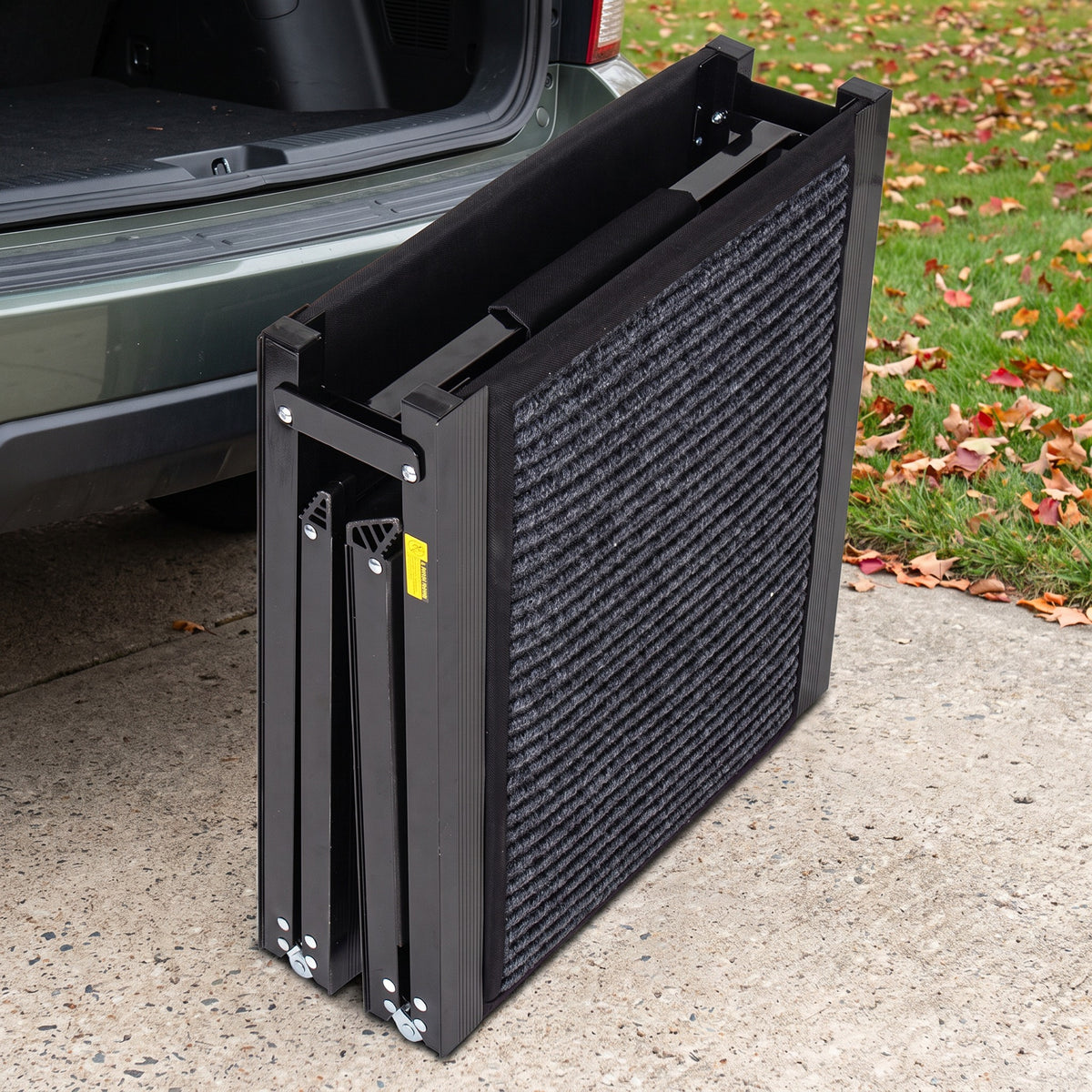 Dog car ramp folded for storage, standing on a driveway next to an SUV